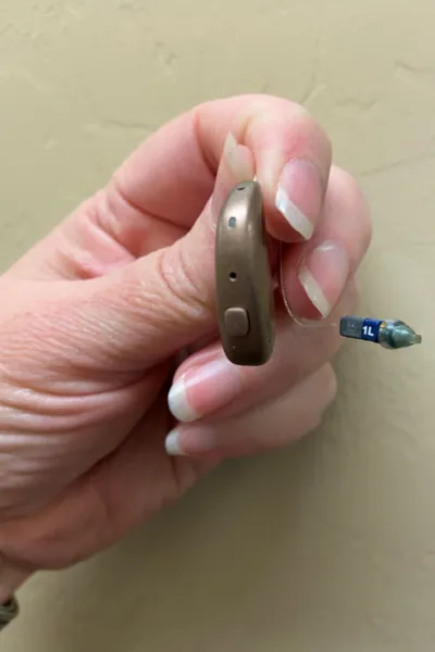A person holding a small, brown hearing aid with a clear tube extending from it.
